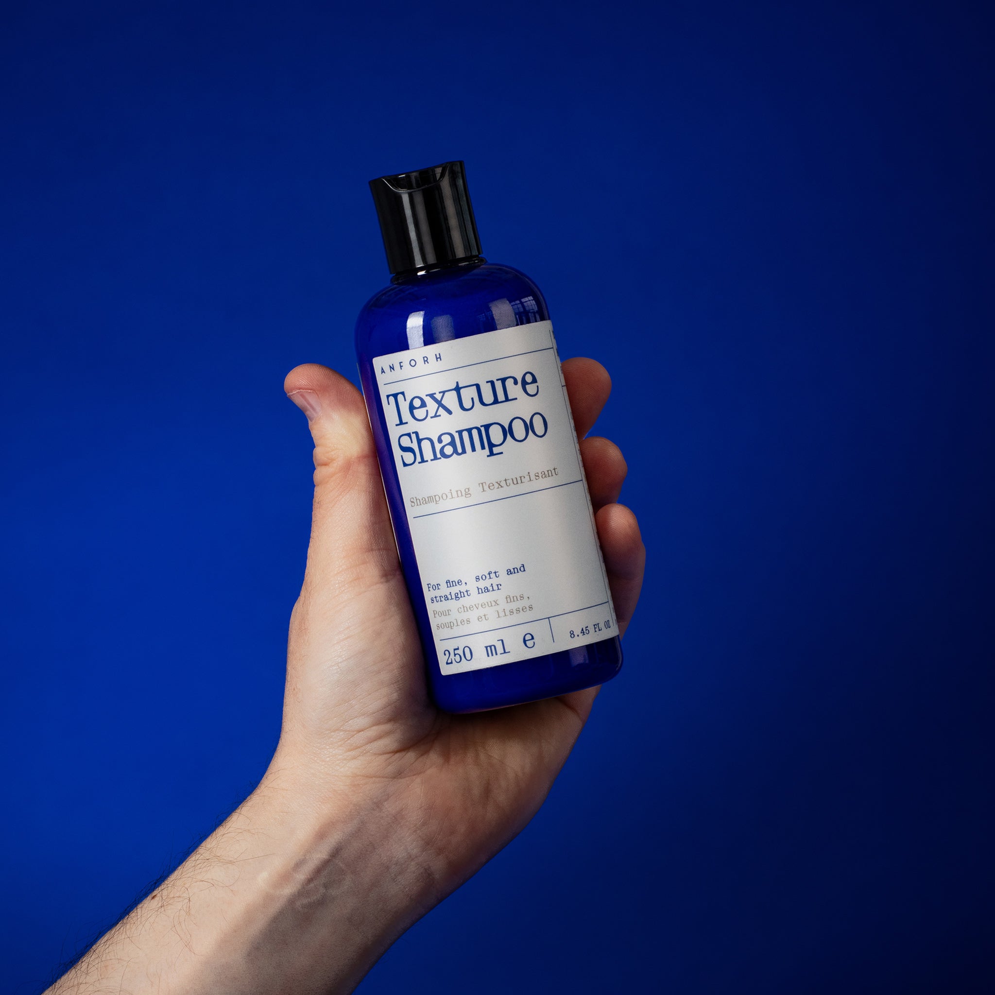 Hand holding the blue plastic bottle of Anforh Texture Shampoo