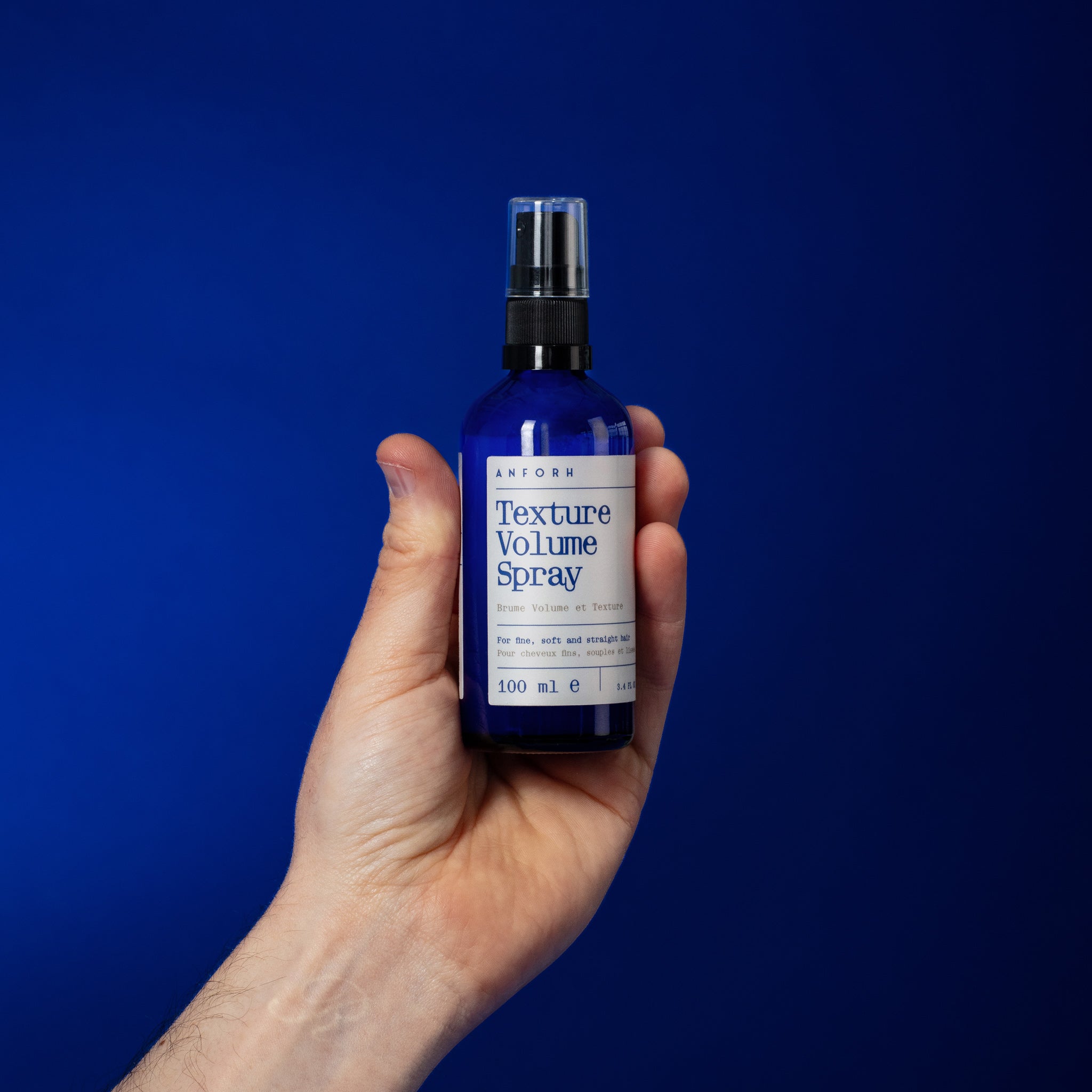 Hand holding the blue glass bottle of Anforh Texture Volume Spray