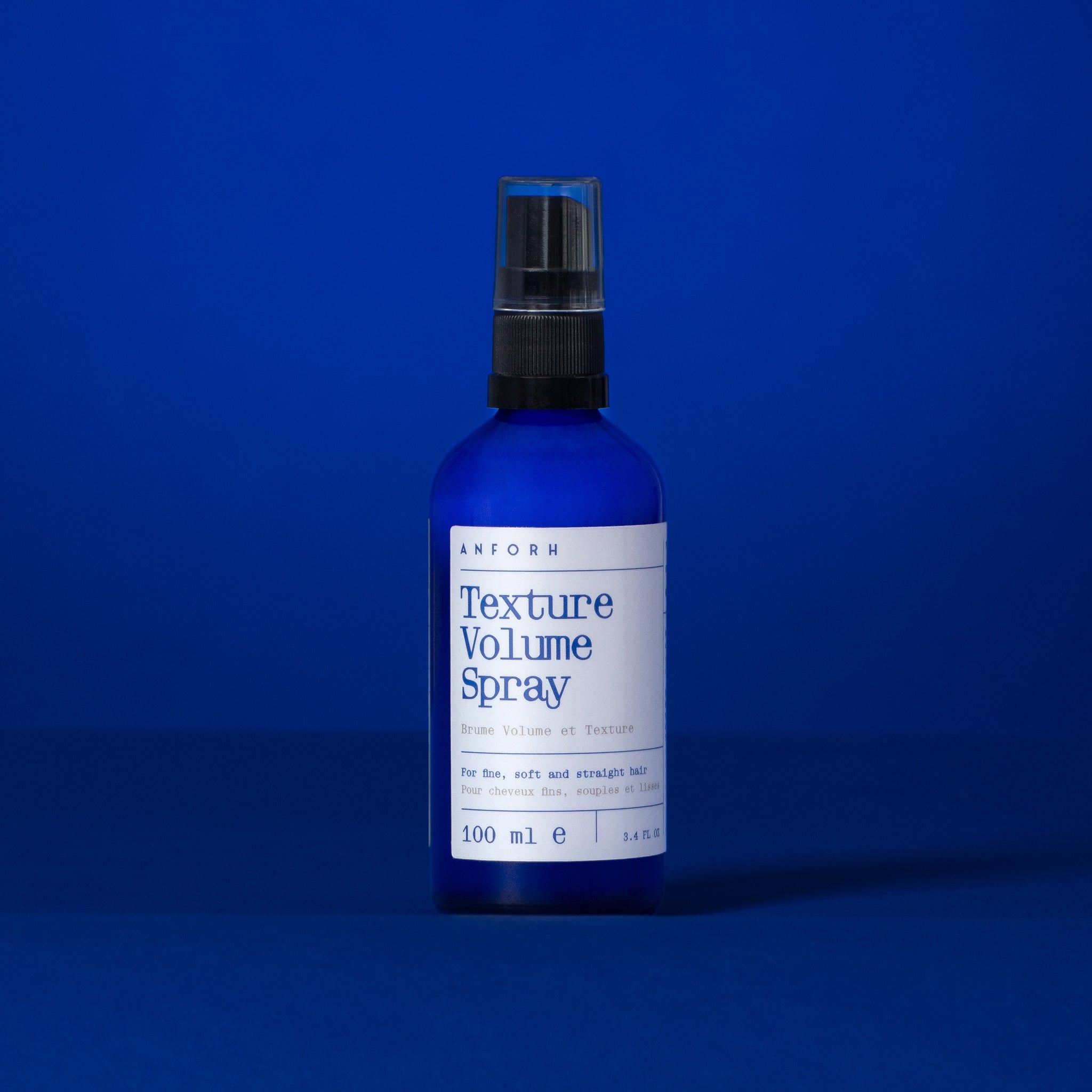Blue glass bottle of Anforh Texture Volume Spray against a blue background