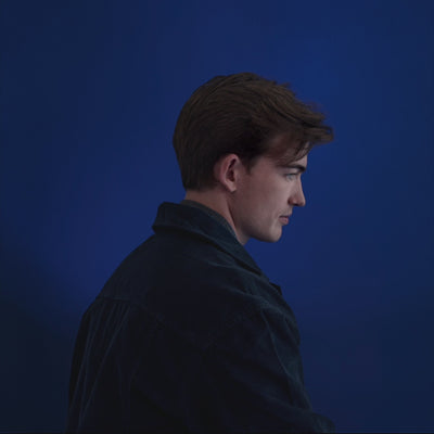 Male model against a blue backdrop lifting his head, showing thicker, textured hair after using Anforh Texture Volume Spray